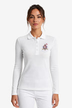 Polo de golf femme manches longues blanc, col boutonné et écusson coloré sur la poitrine.