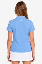 Polo technique fille bleu ciel, vue dos, écusson au col, avec jupe blanche.